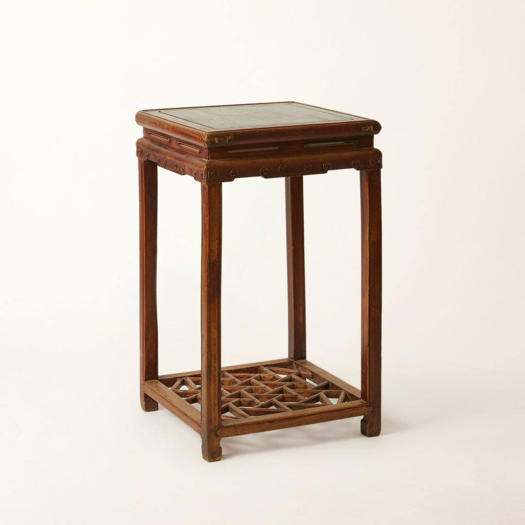 Wooden side table with patinaed top and lattice bottom on a white background