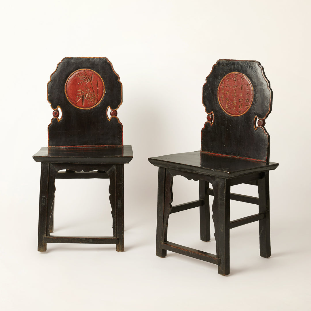 Pair of black Chinese wooden chairs with red mealions on a white background