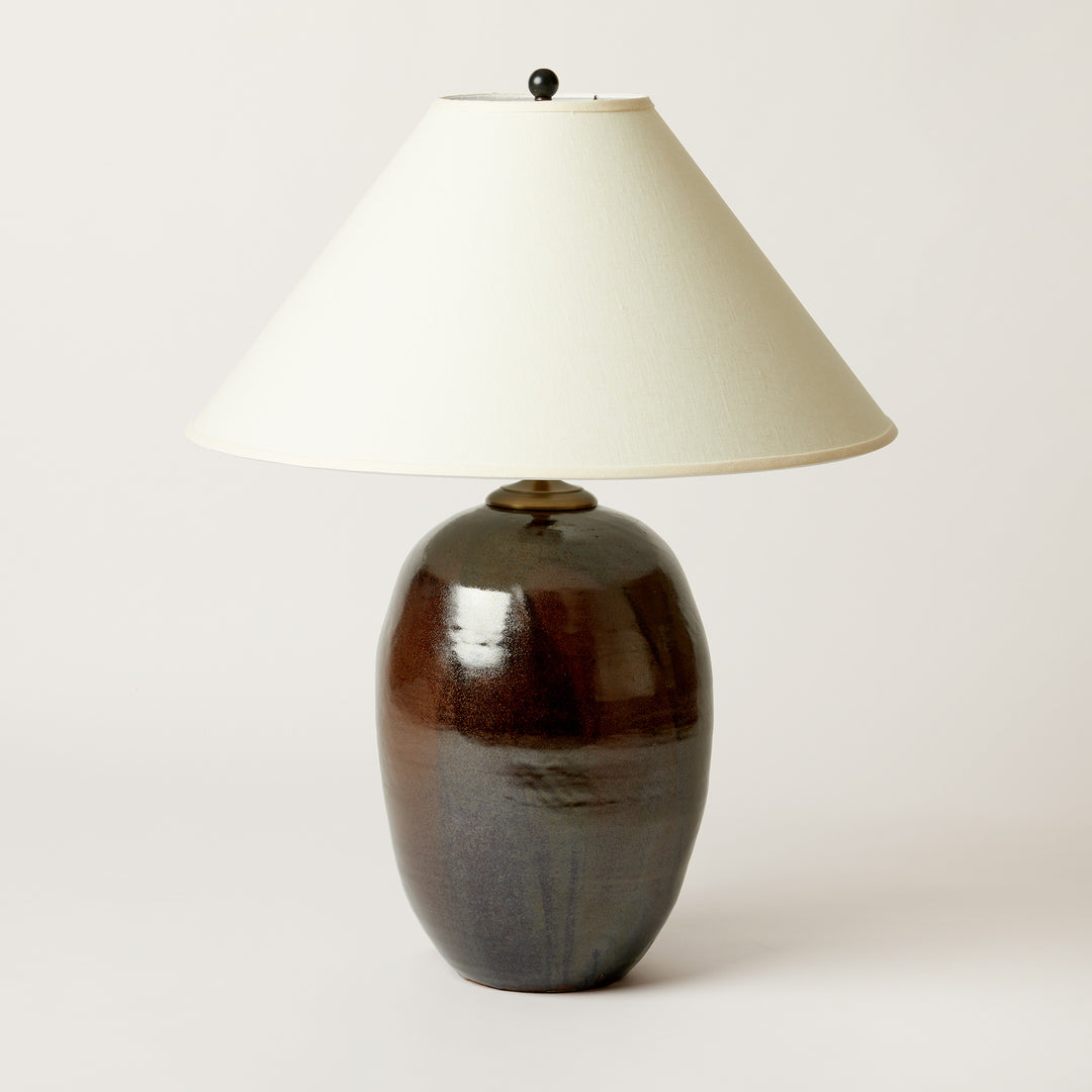 A table lamp with a glossy dark brown ceramic base and a cream-colored fabric cone shade, photographed against a neutral light gray background.
