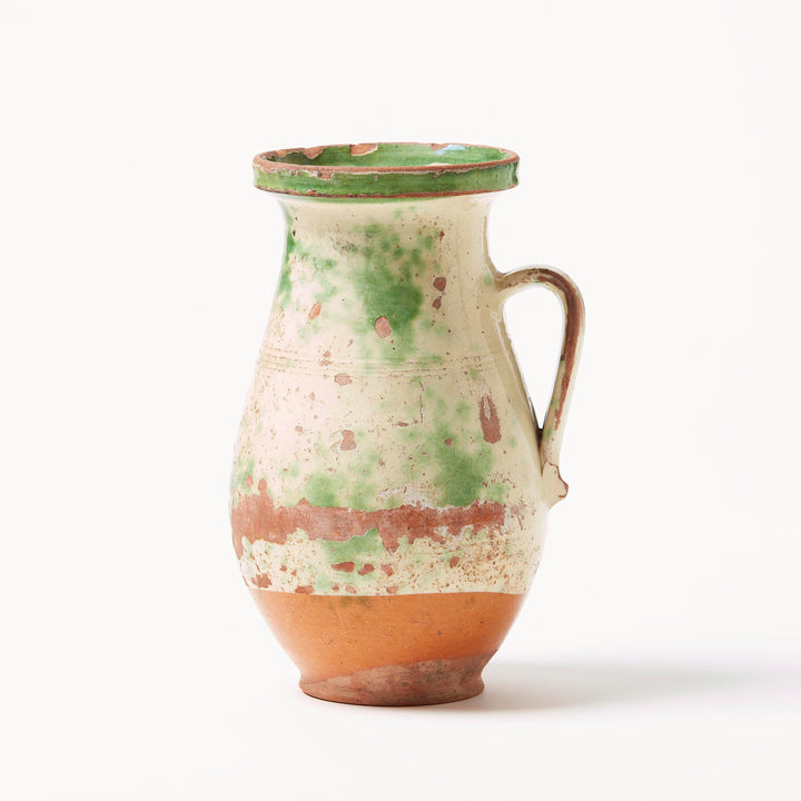 Ceramic pitcher with green and cream glaze on a white background
