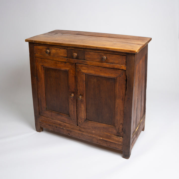 A rustic wooden side cabinet with two lower doors, one top drawer, and round metal knobs, photographed on a light gray studio background.