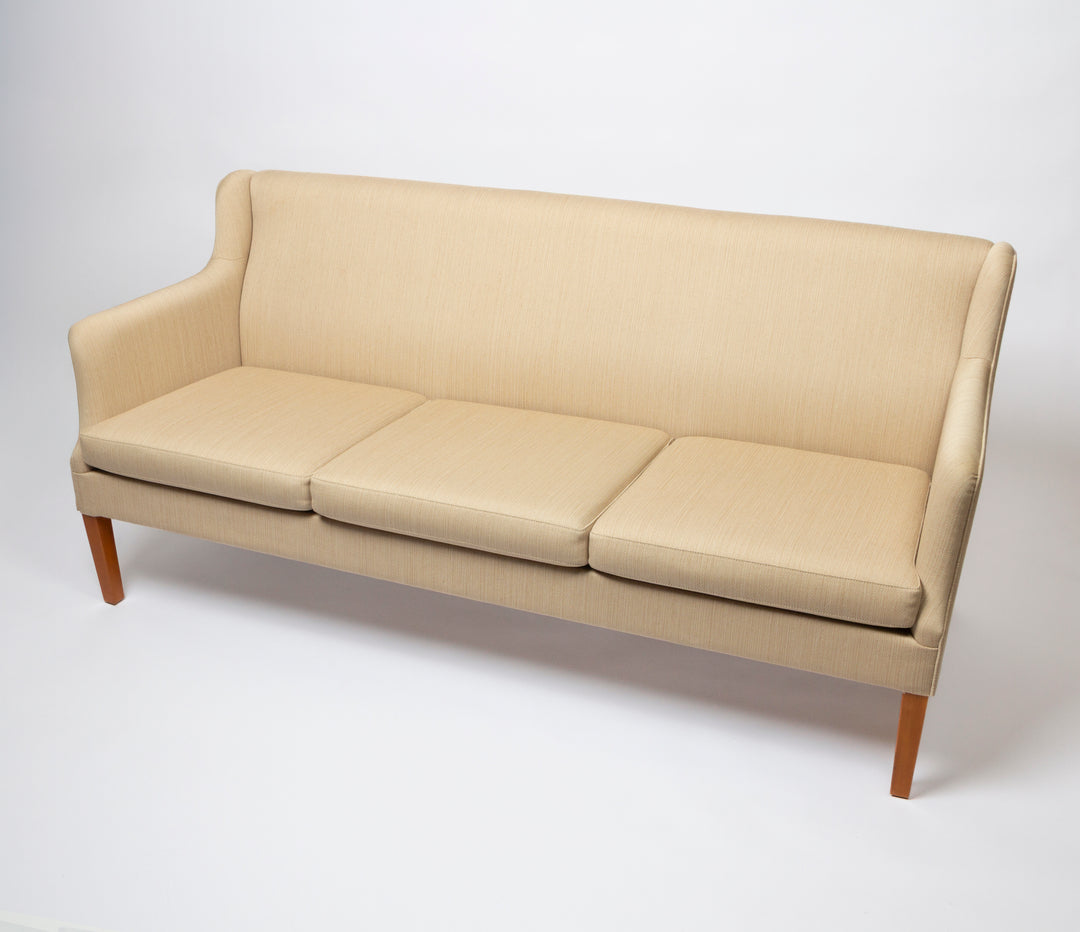 A three-seat upholstered mid-century Danish sofa in a light beige wool fabric with a warm wood finish on the legs, 