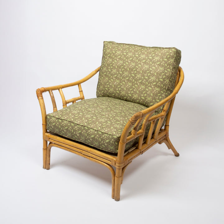 A classic outdoor-style armchair with a natural bamboo frame and thick cushions upholstered in an olive green and beige floral pattern, photographed on a seamless white studio background.