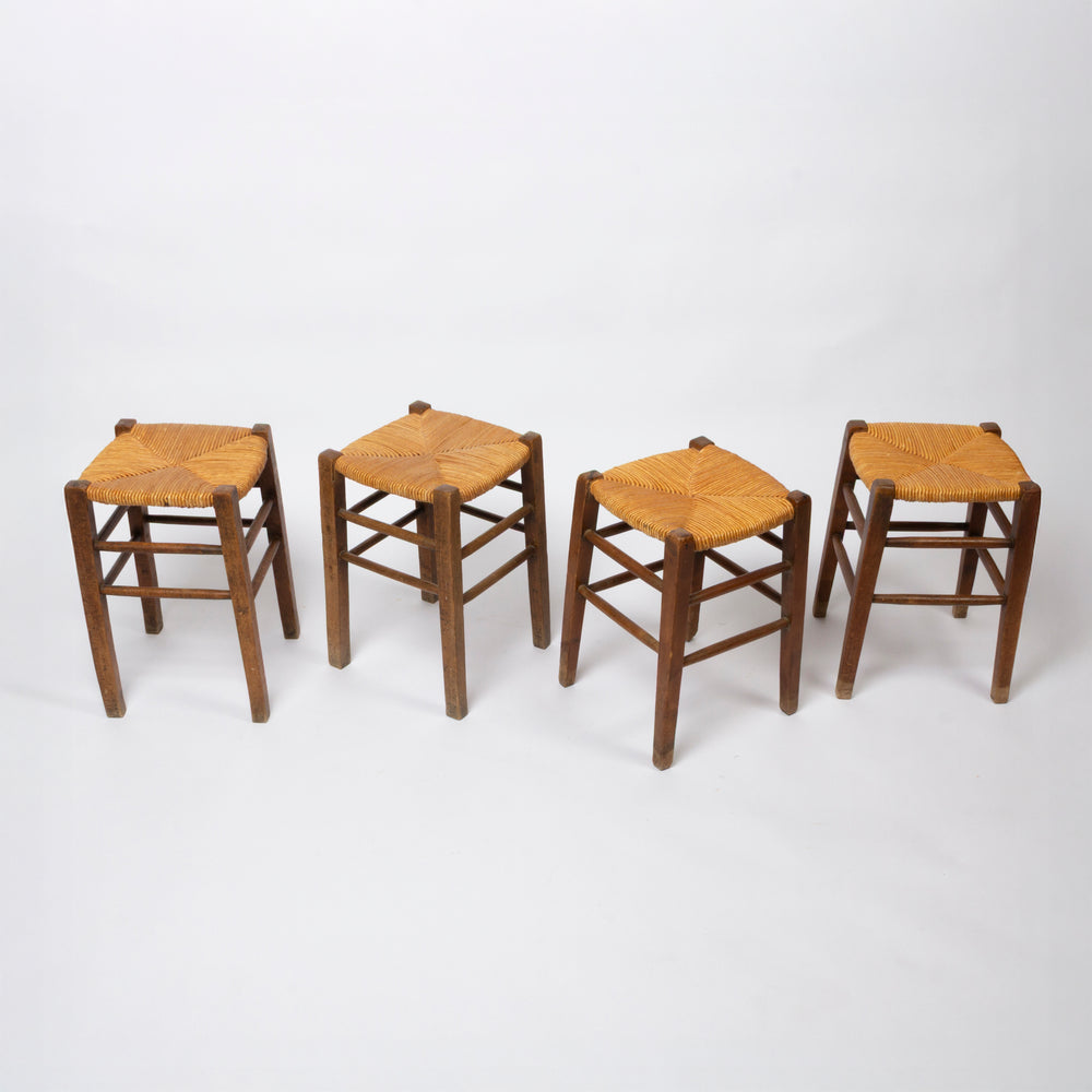 Four wooden stools with woven straw seats, arranged in a row on a plain white studio background.