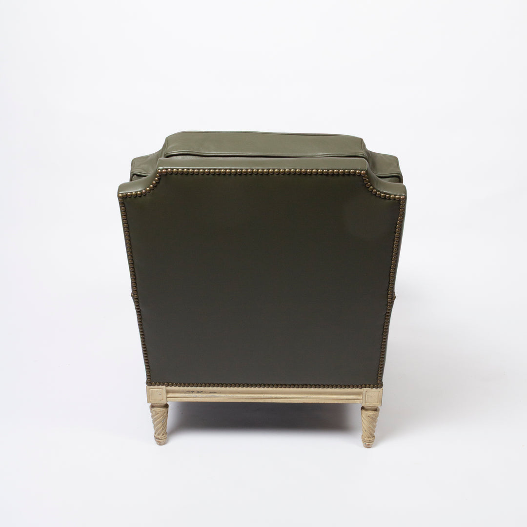 An olive green upholstered armchair shown from the back, featuring brass nailhead trim and turned light wood legs on a white studio background.