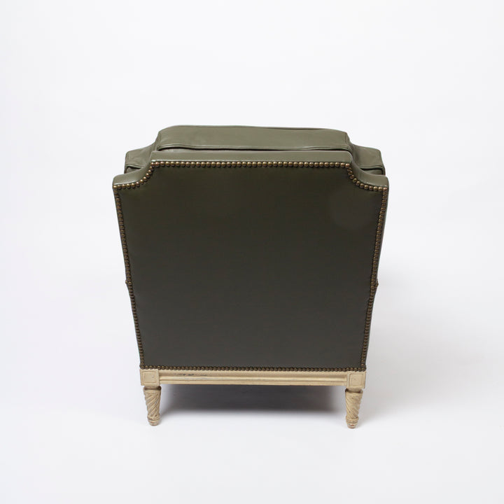 An olive green upholstered armchair shown from the back, featuring brass nailhead trim and turned light wood legs on a white studio background.