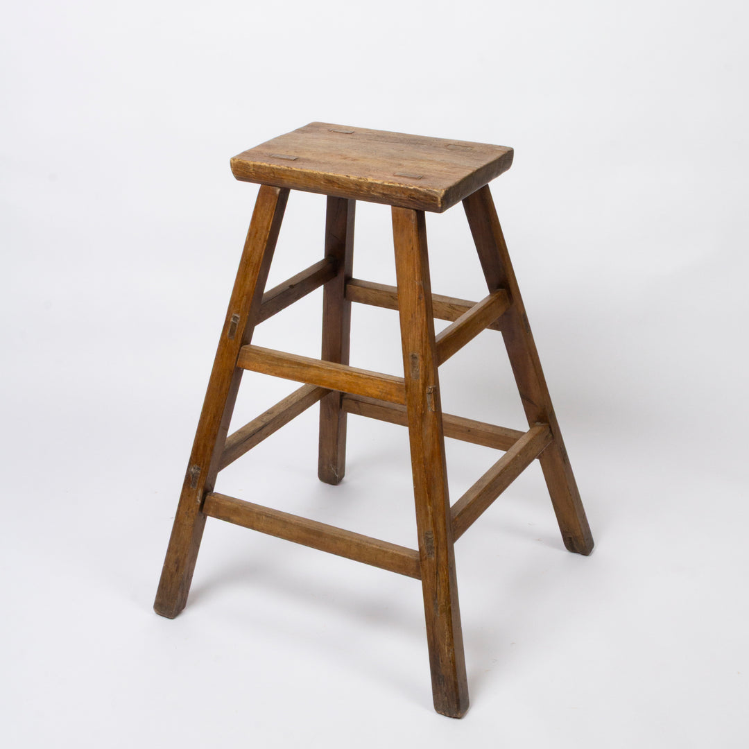 A rustic wooden stool with a square seat and four angled legs connected by three horizontal stretchers, shown on a plain white studio background.