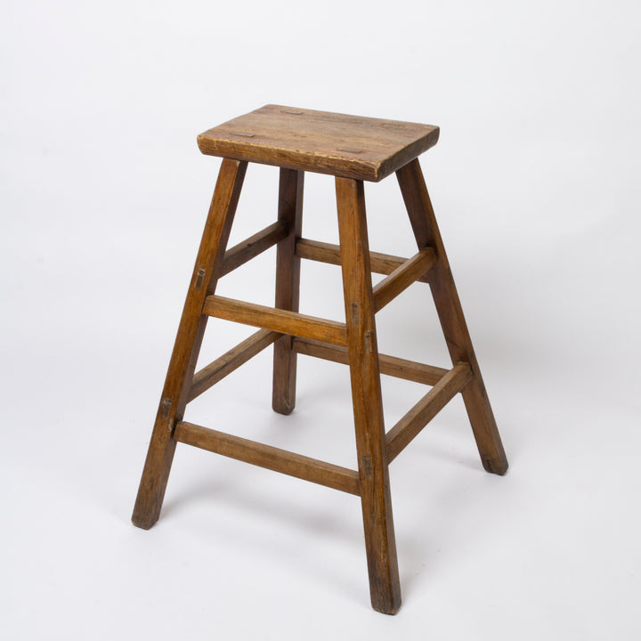 A rustic wooden stool with a square seat and four angled legs connected by three horizontal stretchers, shown on a plain white studio background.