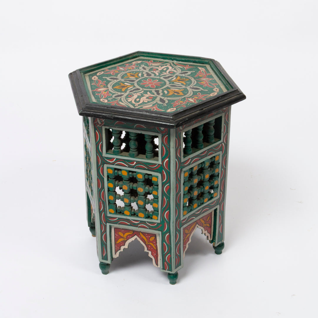 A hexagonal decorative Moroccan wooden side table with intricate hand-painted floral patterns in green, red, orange, and yellow on a white studio background.