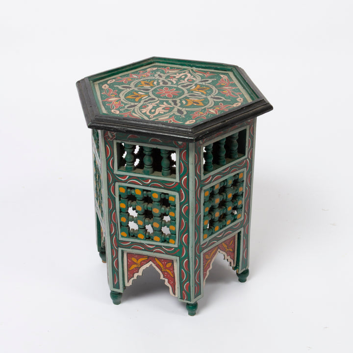 A hexagonal decorative Moroccan wooden side table with intricate hand-painted floral patterns in green, red, orange, and yellow on a white studio background.