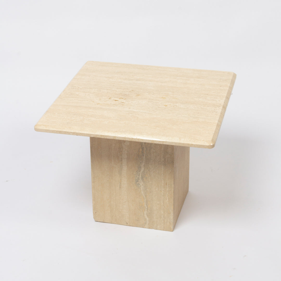 A modern square side table made of light beige travertine stone, featuring a flat top and a solid pedestal base, photographed on a seamless white background.