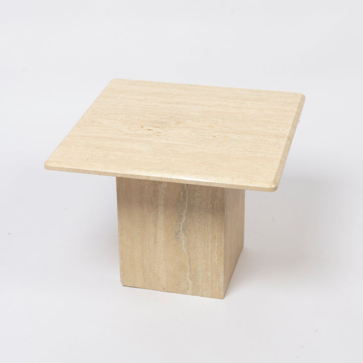 A modern square side table made of light beige travertine stone, featuring a flat top and a solid pedestal base, photographed on a seamless white background.