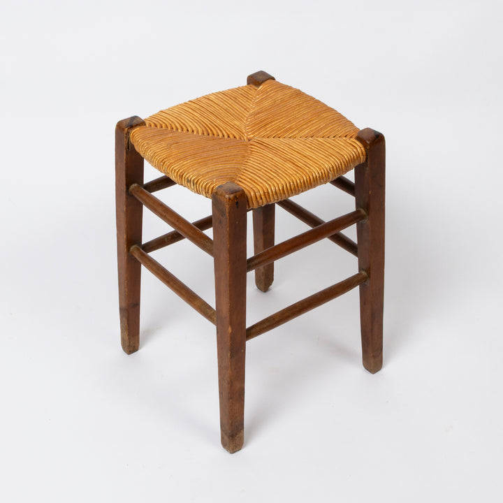 A rustic wooden stool with a square woven rattan or rope seat
