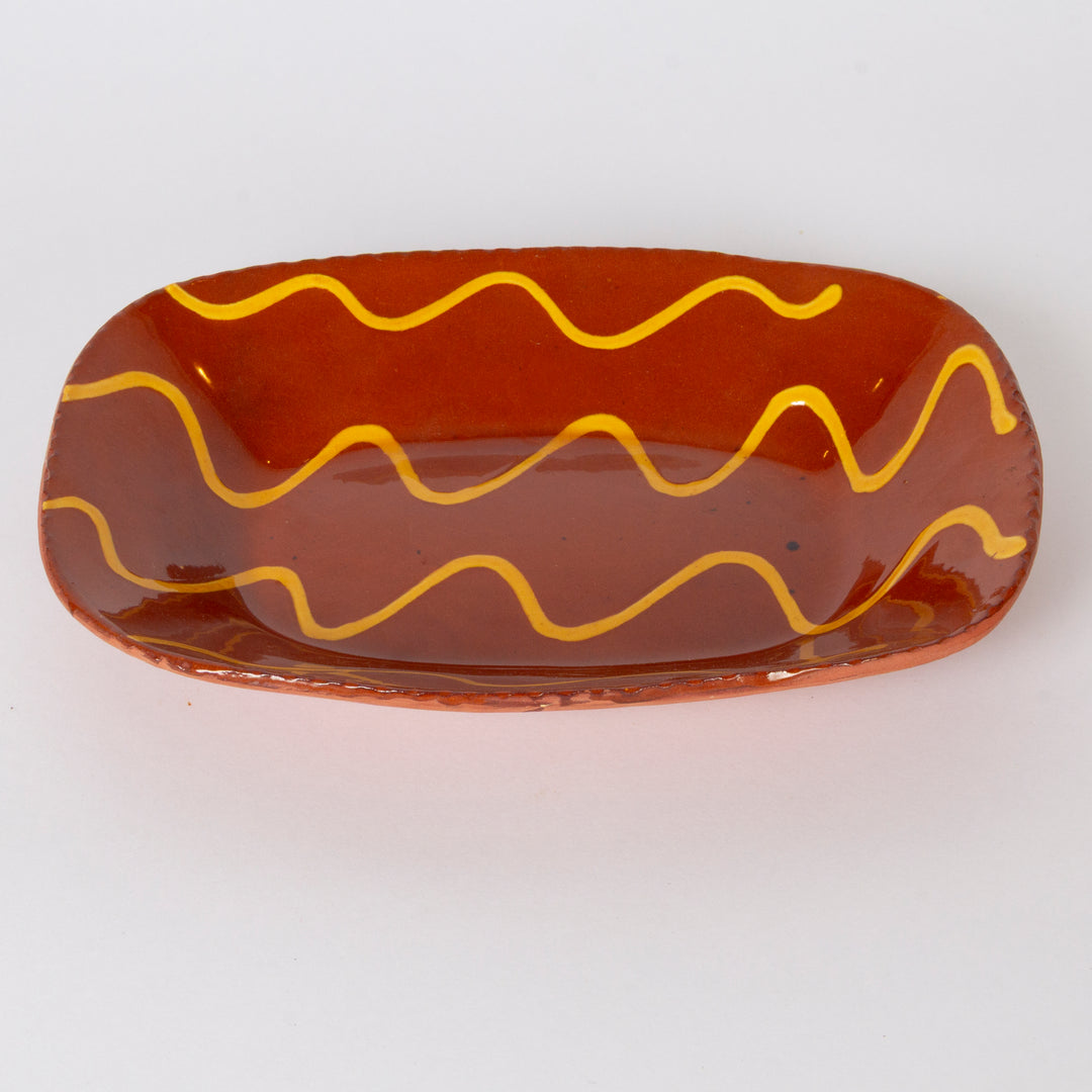 A glossy terracotta-colored ceramic dish with three wavy yellow lines painted across it, shown on a plain white background.