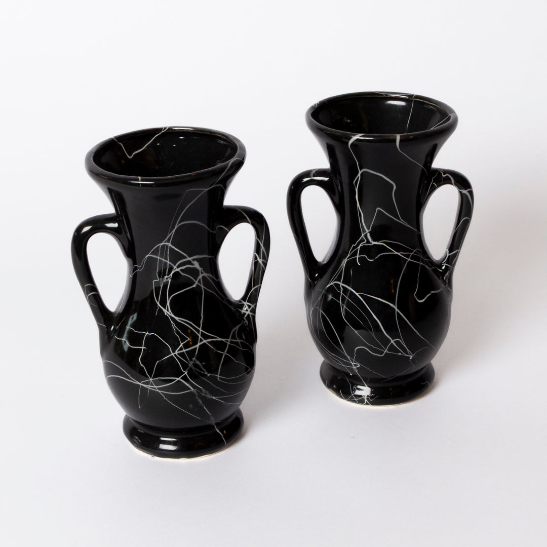 Two glossy black ceramic vases with white marble-like veining, each featuring a double handle and flared rim, displayed on a clean white background.