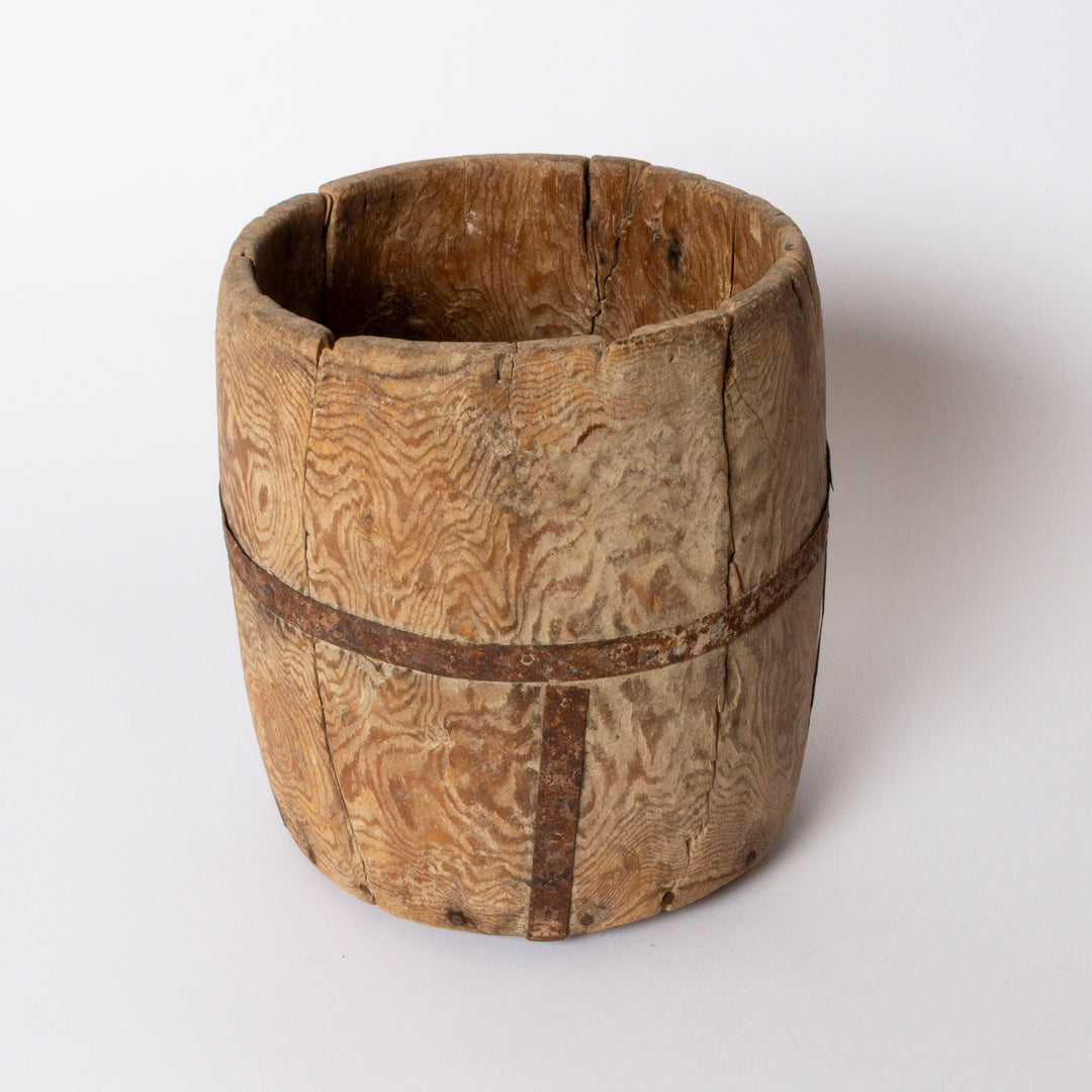 A rustic, vintage wooden bucket or planter made from natural wood planks with visible grain patterns and dark metal bands, photographed on a clean white background.