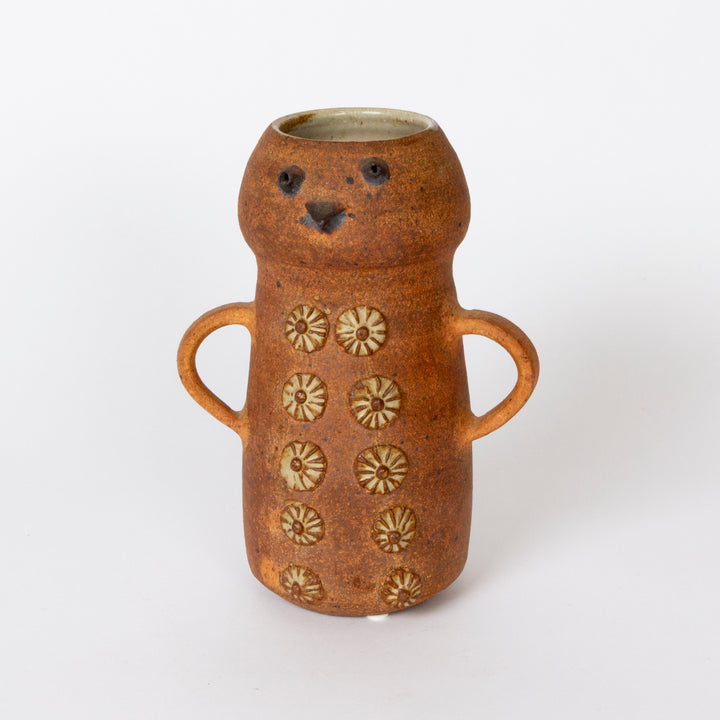 A handmade ceramic vase shaped like a bear, featuring a warm terracotta-brown glaze, two side handles, and raised floral patterns on the front, set against a plain white background.