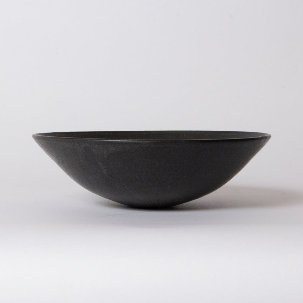 A matte black ceramic bowl with a wide, shallow depth, photographed against a seamless light gray studio background.