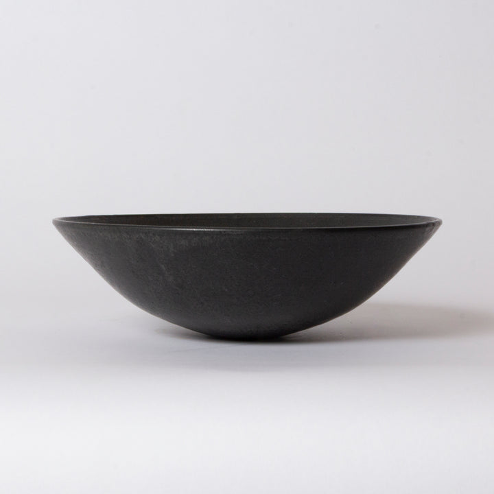 A matte black ceramic bowl with a wide, shallow depth, photographed against a seamless light gray studio background.