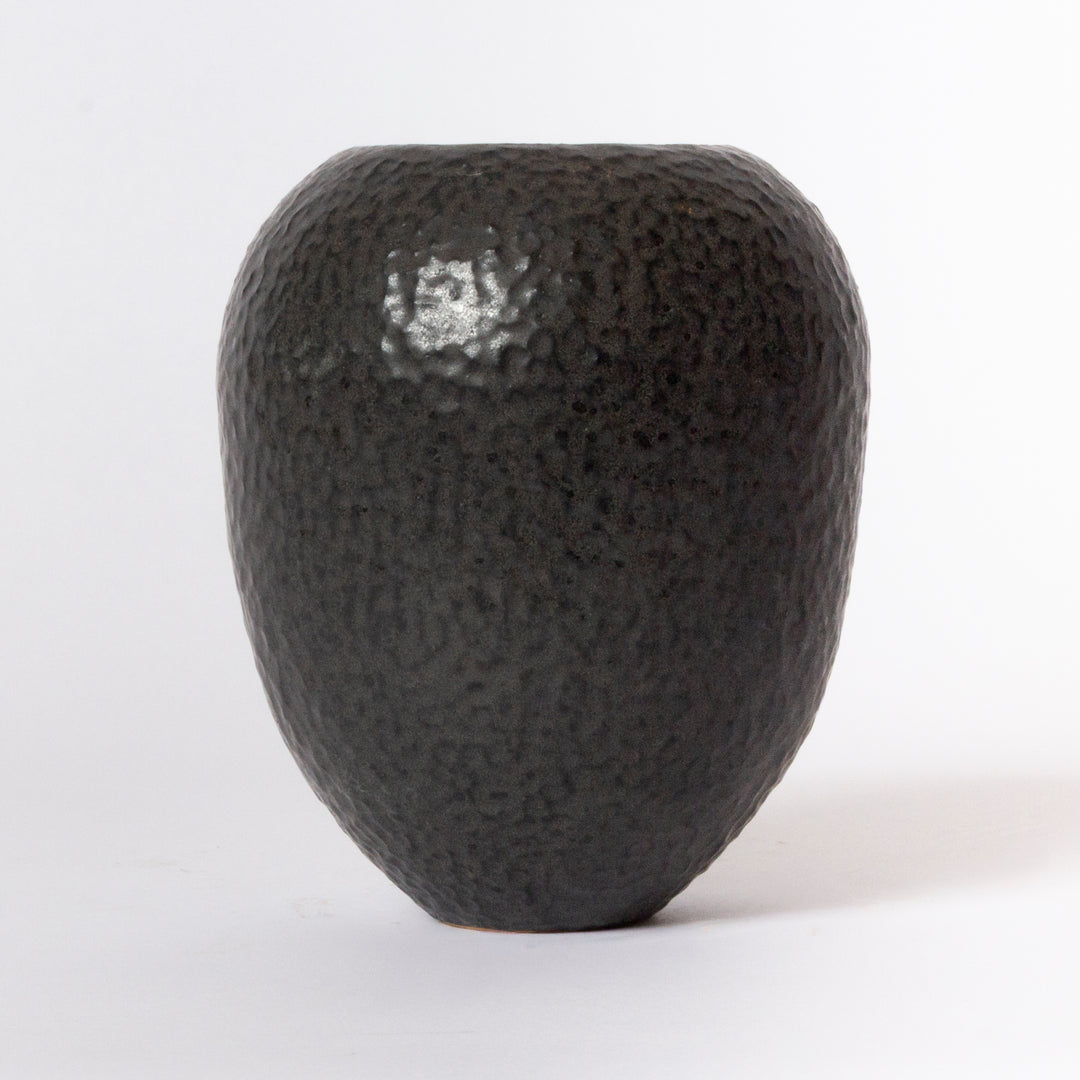 A small, rounded ceramic vase with a dark charcoal black, hammered texture, photographed against a clean white background.