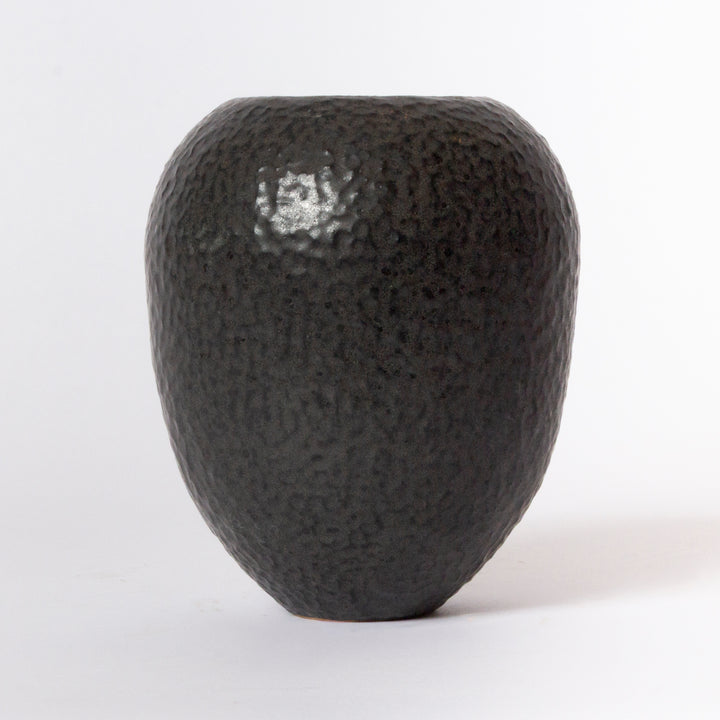 A small, rounded ceramic vase with a dark charcoal black, hammered texture, photographed against a clean white background.