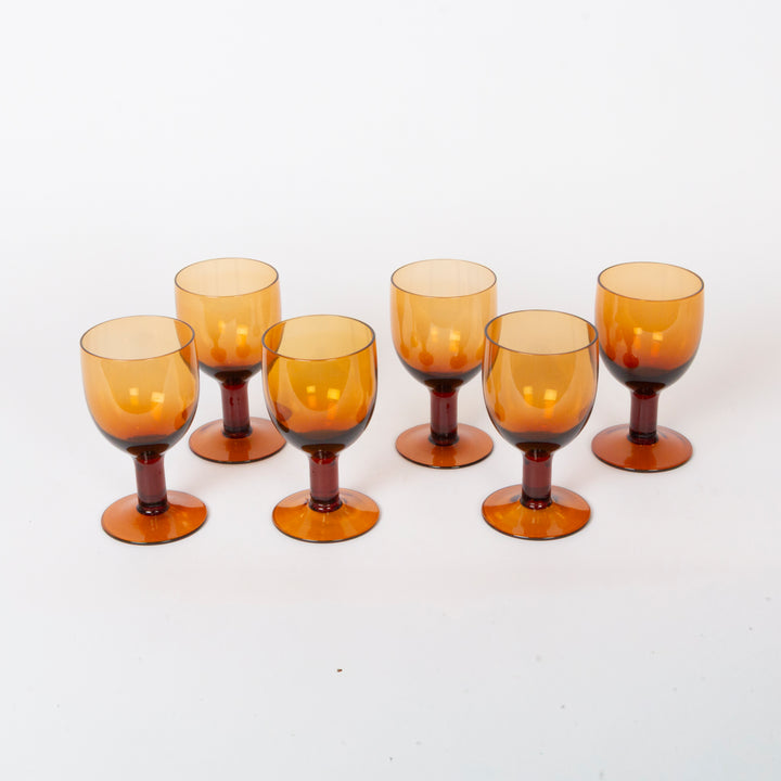 Six amber-colored glass goblets with a dark brown base, arranged on a plain white background.
