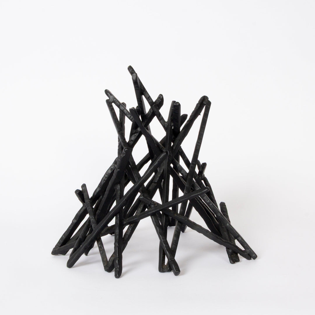 A black twig-style decorative sculpture or miniature campfire structure made of many thin intersecting sticks, photographed on a clean white studio background.