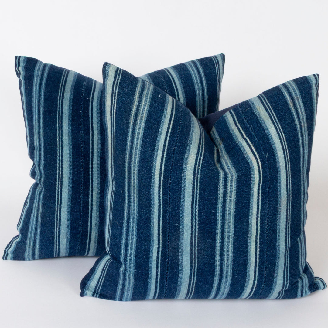 Two square throw pillows with vertical indigo blue and white stripes, arranged against a plain white background.