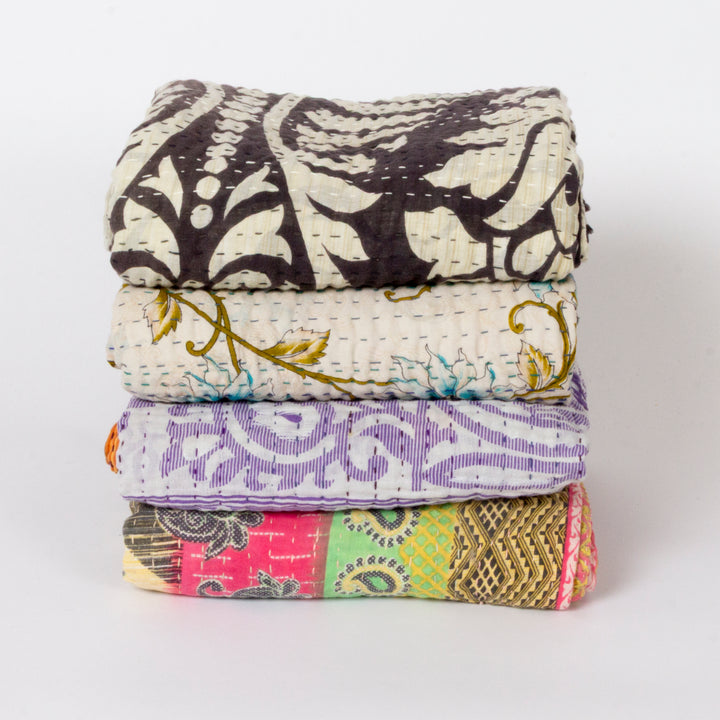 A stack of four folded cotton kantha quilts with various colorful and patterned designs, photographed on a clean white background.