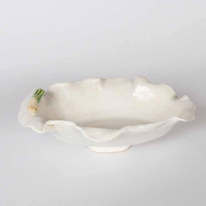 An off-white ceramic serving bowl with a wavy, scalloped rim and a small sculpted onion detail on the left side, set against a plain light gray background.