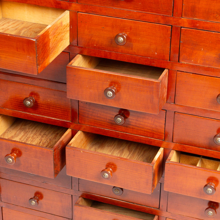A close-up of a wooden drawer cabinet with multiple reddish-brown drawers, some pulled open to show the interior, and round metal knobs.