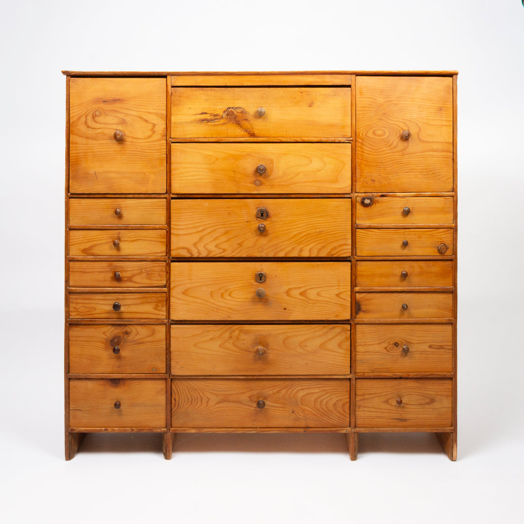 A wooden chest of drawers with multiple drawers and two cabinet doors, made of warm-toned pine wood with visible grain and small round knobs, photographed against a plain white studio background.