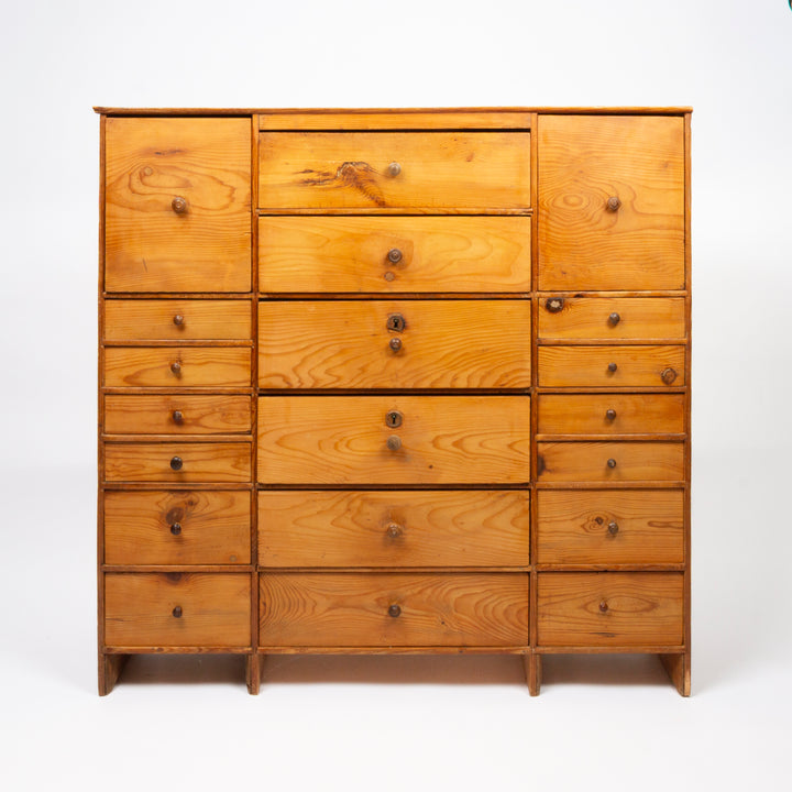 A wooden chest of drawers with multiple drawers and two cabinet doors, made of warm-toned pine wood with visible grain and small round knobs, photographed against a plain white studio background.