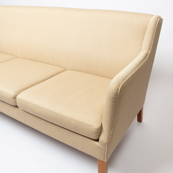 A close-up of a modern upholstered sofa in a light beige fabric, showing the backrest, seat cushions, armrest, and wooden legs against a clean white background.