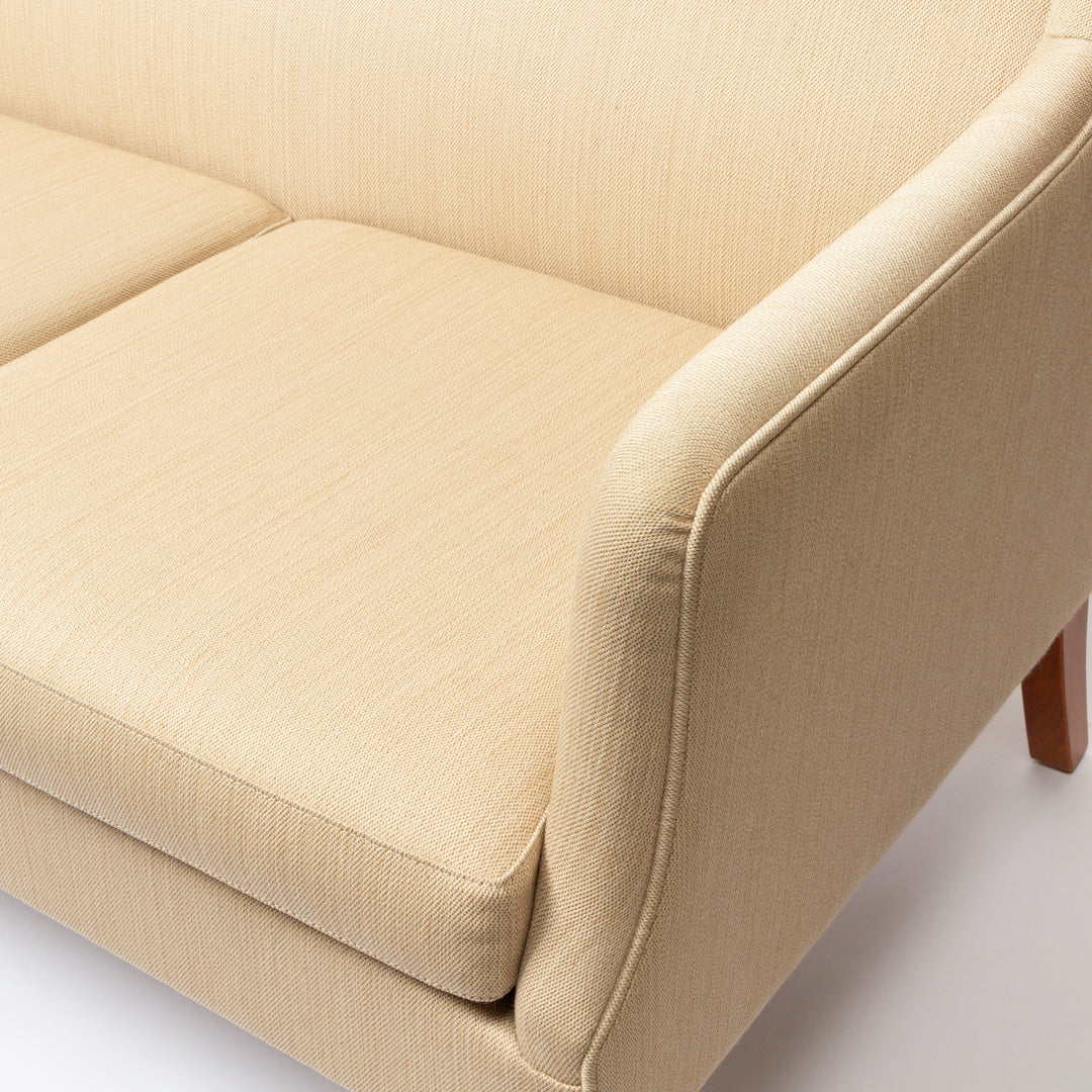 Close-up of a beige upholstered sofa showing the seat cushion, backrest, armrest, and a small portion of a wooden leg on a clean white background.