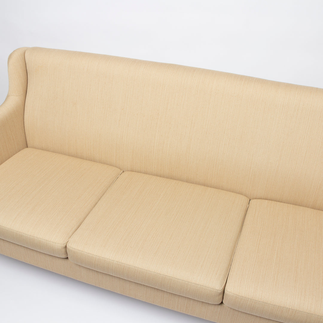 A close-up of a beige upholstered sofa with three seat cushions and a tall backrest, shown against a plain white background.