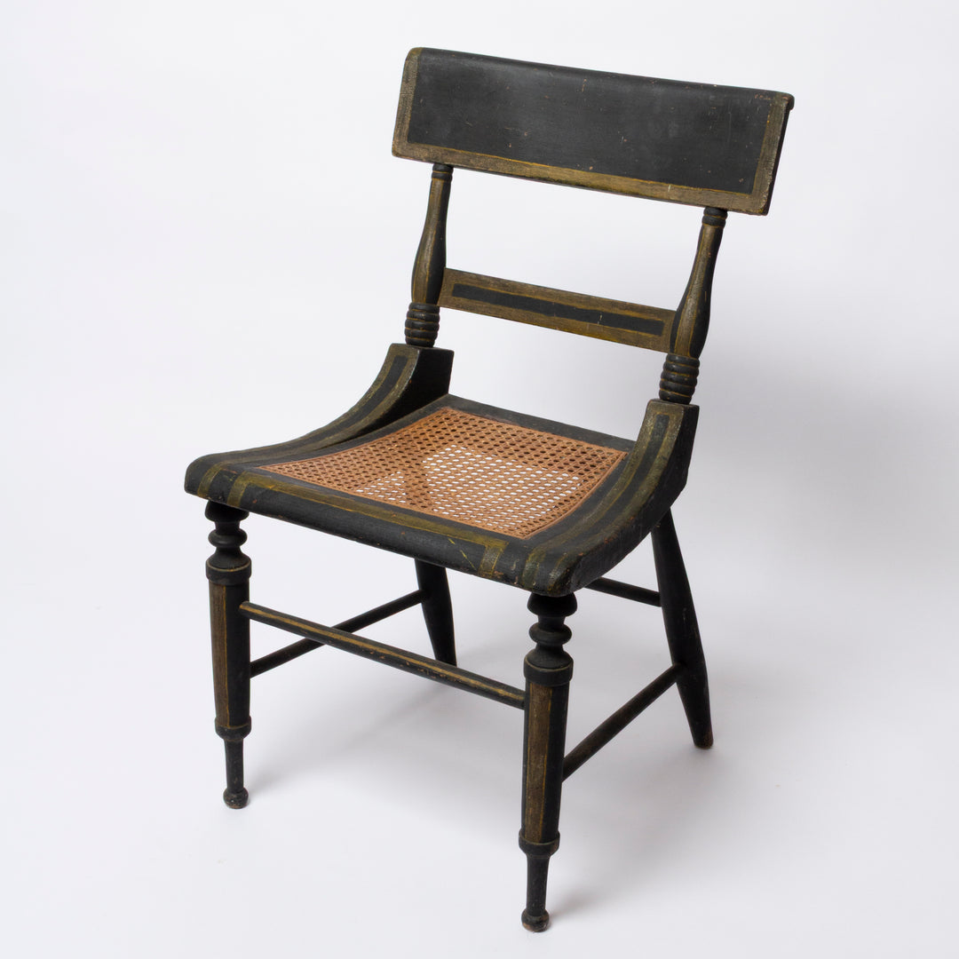 A vintage wooden dining chair with a dark painted frame and a woven cane seat, shown on a plain white studio background.