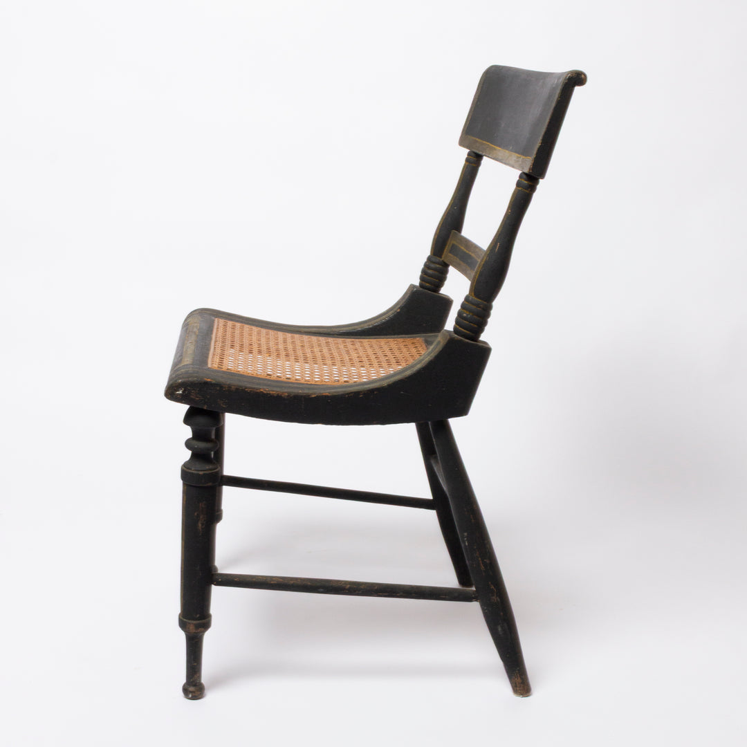 A vintage wooden dining chair with a black painted frame and a natural woven cane seat and backrest, shown from a three-quarter angle on a white background.