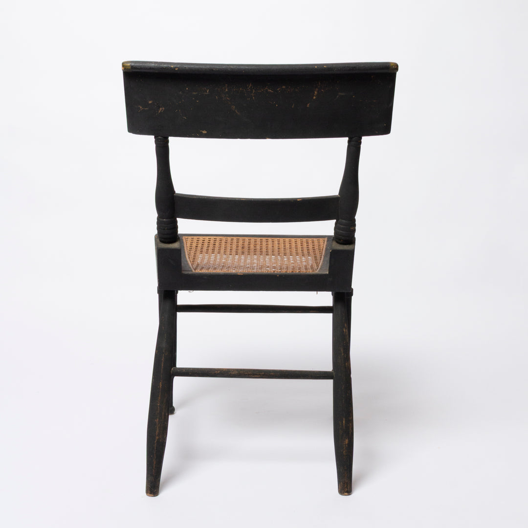 A vintage black wooden chair with a woven cane seat, shown from the back against a plain white background.