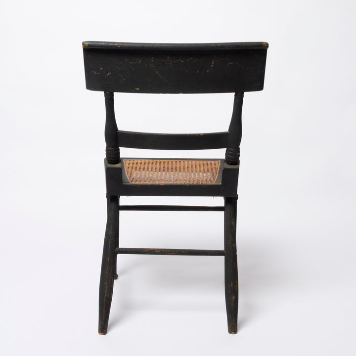A vintage black wooden chair with a woven cane seat, shown from the back against a plain white background.
