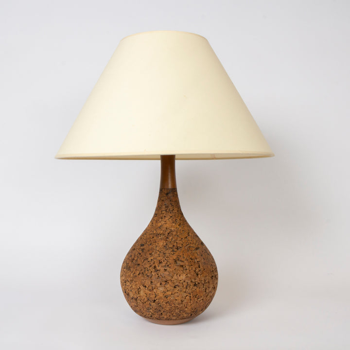 A 1960s table lamp with a tapered off-white fabric shade and a teardrop-shaped cork base, photographed against a plain light gray background.