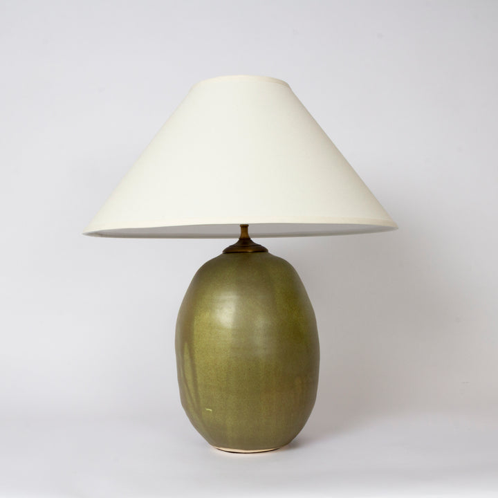 A table lamp with a glossy olive green ceramic base and a conical off-white fabric shade, photographed against a neutral light gray background.